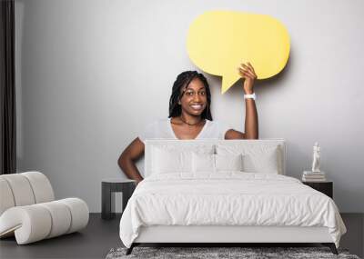 Portrait of a happy young african woman holding empty speech bubble isolated over gray background Wall mural